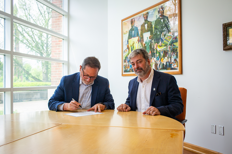 Two men sit at a table signing a document. 